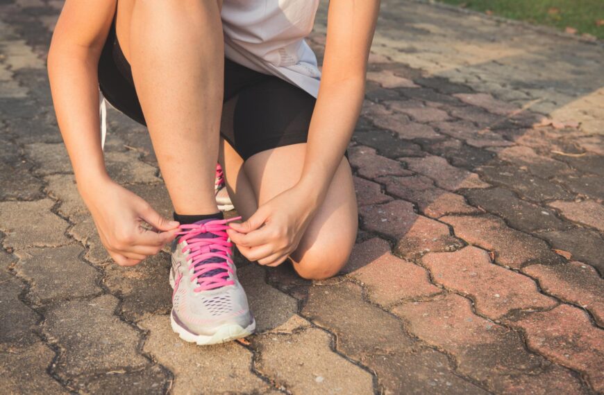 woman lacing up her gray and pink nike low top athletic shoe